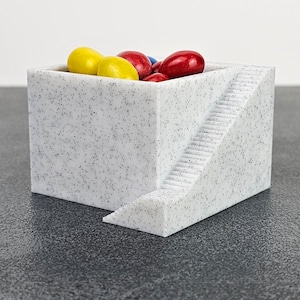 Könnte beinhalten: Ein weißer, gesprenkelter Keramikbehälter mit Treppenstufen-Design. Der Behälter ist mit roten, gelben und blauen Süßigkeiten gefüllt.