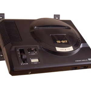 May include: A black Sega Mega Drive 16-bit video game console with a grey and black controller. The console has a slot for a game cartridge and a CD drive. The console is labelled "MEGA DRIVE SEGA" and "16-BIT".