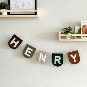 Custom felt name banner with scallop flags, strung on white twine, displayed on a nursery wall