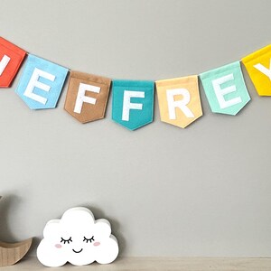 Personalized felt bunting banner with baby name, hanging in a neutral nursery