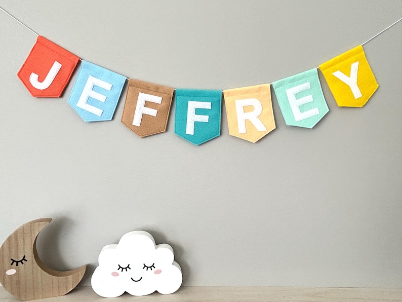Personalized felt bunting banner with baby name, hanging in a neutral nursery