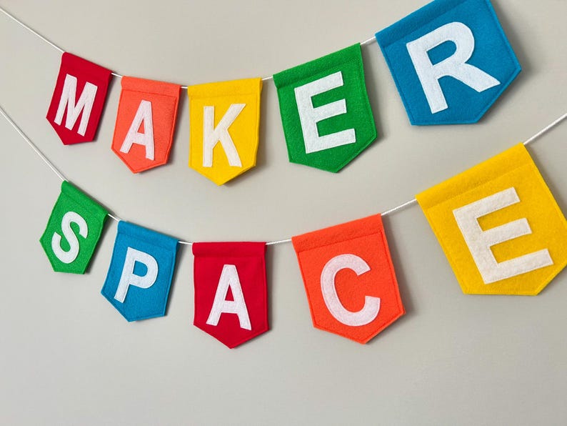 Puede incluir: Una colorida guirnalda de fieltro que deletrea "MAKER SPACE" con letras blancas. Las banderolas son rojas, naranjas, amarillas, verdes, azules y naranjas. La guirnalda est&aacute; ensartada en una cuerda blanca, perfecta para una sala de manualidades.