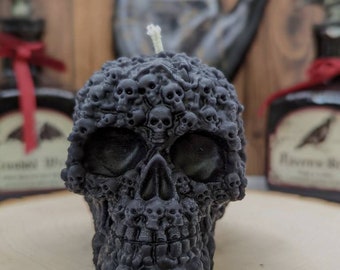 May include: Black skull candle with a detailed design of smaller skulls. The candle is made of wax and has a white wick.