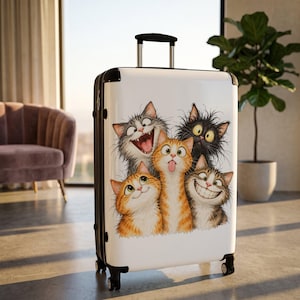 May include: A white hard-shell rolling suitcase featuring a colorful graphic illustration of five cats with various expressive faces, including wide grins, a tongue sticking out, and wide eyes, set against a clean white background.