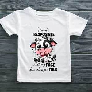 May include: White t-shirt with a cartoon cow and the text "I'm not responsible for what my face does when you talk."