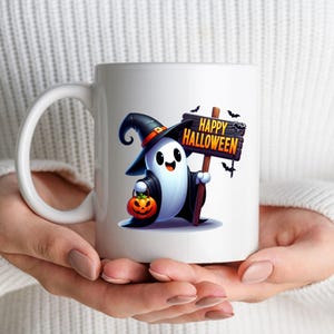 K&ouml;nnte beinhalten: Wei&szlig;e Keramiktasse mit einem Cartoon-Geist, der einen Hexenhut tr&auml;gt und ein Schild mit der Aufschrift "Happy Halloween" h&auml;lt. Der Geist tr&auml;gt einen K&uuml;rbis.