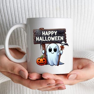 K&ouml;nnte beinhalten: Eine wei&szlig;e Keramik-Kaffeetasse mit einem Cartoon-Geist, der ein Schild mit der Aufschrift "Happy Halloween" h&auml;lt. Der Geist h&auml;lt einen Stock mit einem Sch&auml;del und einer Fledermaus darauf. In der Ecke des Bildes befindet sich ein K&uuml;rbis.