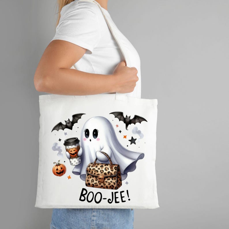 May include: White tote bag with a cartoon ghost holding a coffee cup and a leopard print purse. The ghost has big eyes and a cute expression. The bag also has bats and stars printed on it. The text "BOO-JEE!" is printed on the bottom of the bag.