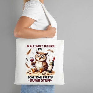 Op de afbeelding: Witte tote bag met een cartoon uil die wijn drinkt en de tekst "In de verdediging van alcohol heb ik een aantal behoorlijk domme dingen gedaan."