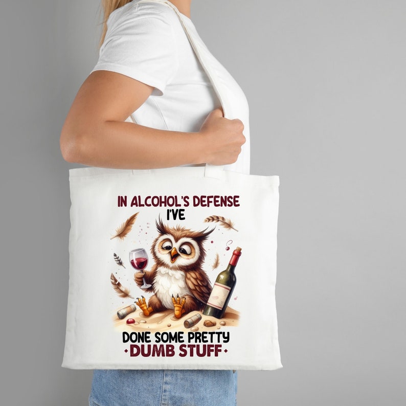 Op de afbeelding: Witte tote bag met een cartoon uil die wijn drinkt en de tekst "In de verdediging van alcohol heb ik een aantal behoorlijk domme dingen gedaan."