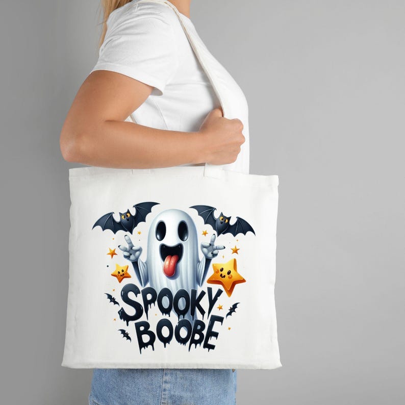 May include: White tote bag with a cartoon ghost with a tongue sticking out, two bats, and stars. The text "Spooky Boobe" is printed on the bag.