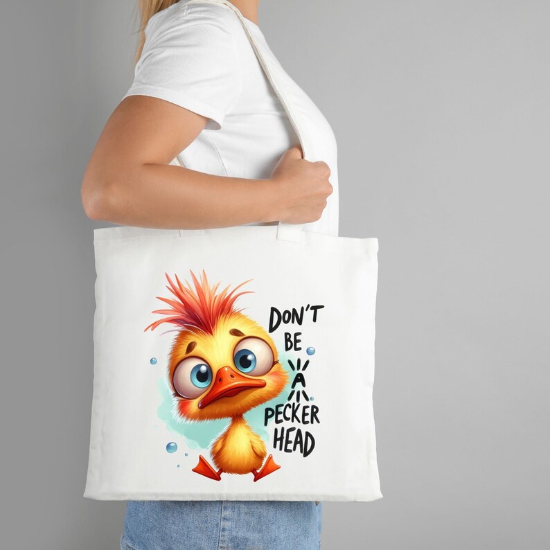 Puede incluir: Bolsa de tela blanca con un pollito amarillo de dibujos animados con plumas rojas y ojos azules. El pollito est&aacute; mirando hacia abajo y el texto "Don't be a pecker head" est&aacute; impreso en la bolsa.