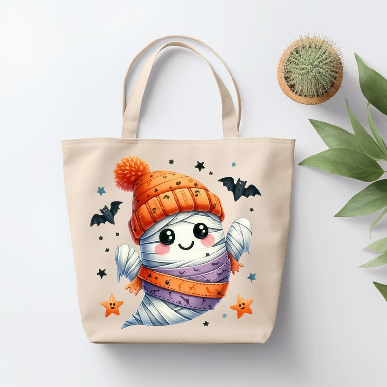 May include: A beige canvas tote bag with a cute cartoon ghost wearing an orange and white hat. The ghost is smiling and has a purple and orange scarf. The bag has black bats and stars printed on it.