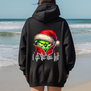 May include: A black hooded sweatshirt featuring a graphic on the back of a green creature wearing a red Santa hat and a red zippered hoodie. Below the graphic, the text reads "I ate the nice list" in a white, stylized cursive font.