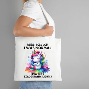 Op de afbeelding: Witte tote bag met een regenboog-eenhoornillustratie en de tekst "Toen ik je vertelde dat ik normaal was, heb ik misschien een beetje overdreven."