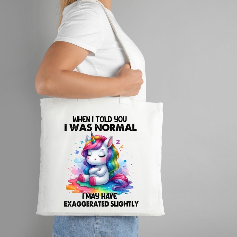 Op de afbeelding: Witte tote bag met een regenboog-eenhoornillustratie en de tekst "Toen ik je vertelde dat ik normaal was, heb ik misschien een beetje overdreven."