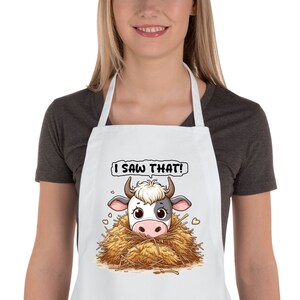 May include: White apron with a cartoon cow peeking out of a pile of hay. The text "I saw that!" is above the cow.
