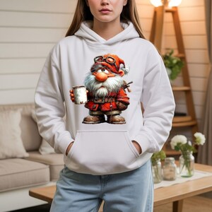 May include: A white hooded sweatshirt featuring a graphic print of a bearded gnome wearing a red coat, brown boots, and goggles on a hat. The gnome has a large nose and holds a white mug. The hoodie has long sleeves and a front kangaroo pocket.