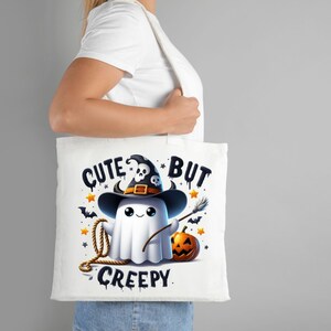 May include: White tote bag with a cute ghost wearing a witch hat and holding a broom. The text on the bag reads "Cute But Creepy".