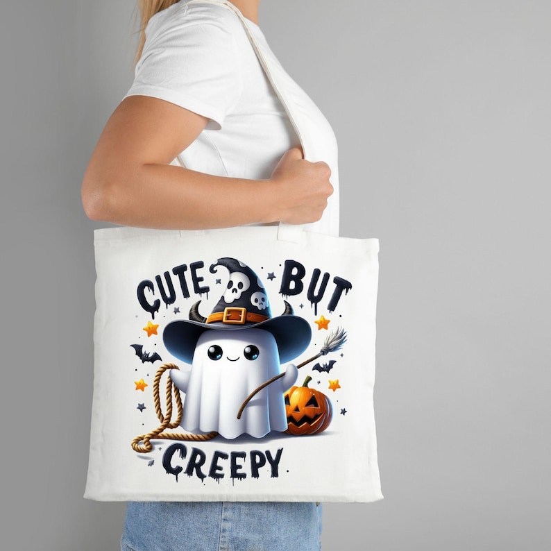 May include: White tote bag with a cute ghost wearing a witch hat and holding a broom. The text on the bag reads "Cute But Creepy".