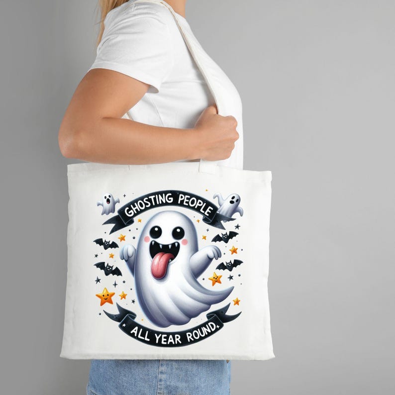 May include: White tote bag with a cartoon ghost with a tongue sticking out. The ghost is surrounded by bats and stars. The text on the bag reads "Ghosting people all year round."