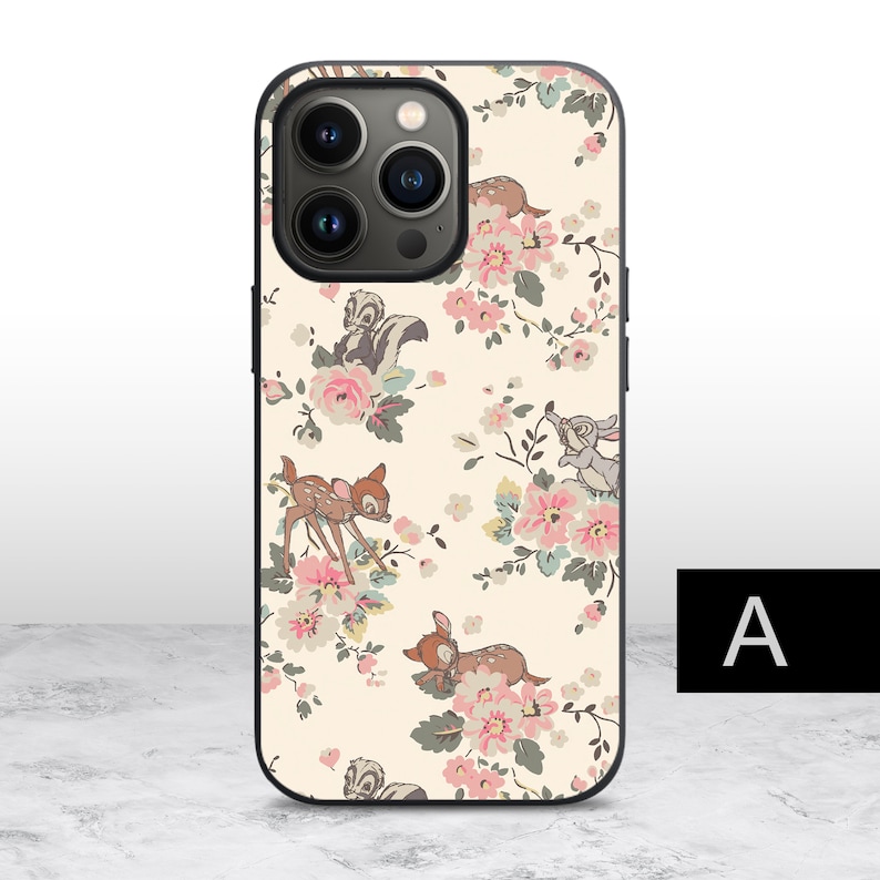 K&ouml;nnte beinhalten: Eine wei&szlig;e Handyh&uuml;lle mit einem Blumenmuster mit Bambi, Klopfer und einem Blumenmuster. Die H&uuml;lle hat eine schwarze Kameraerhebung mit drei Objektiven.