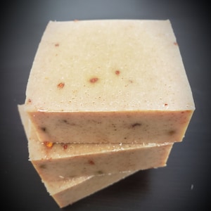 May include: Three bars of beige soap with flecks of brown and red. The soap is stacked on top of each other.