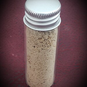 May include: A small glass jar with a silver lid filled with a light beige powder.