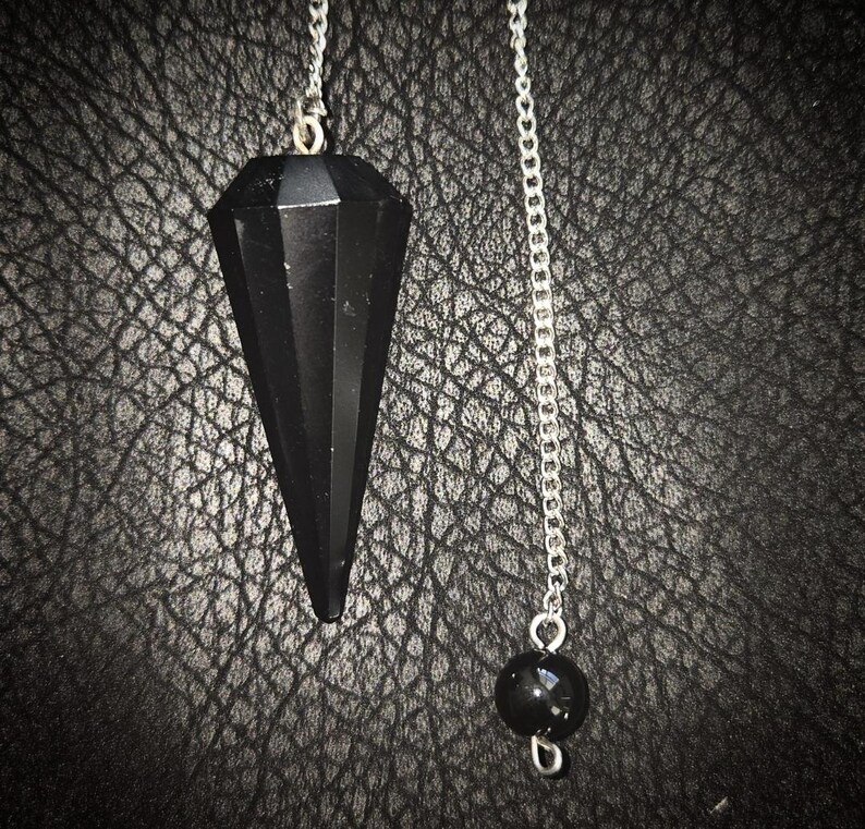 Peut inclure: Un pendule en cristal noir avec une cha&icirc;ne argent&eacute;e. Le pendule est pointu et pr&eacute;sente un design facett&eacute;. La cha&icirc;ne a une petite perle noire &agrave; son extr&eacute;mit&eacute;.