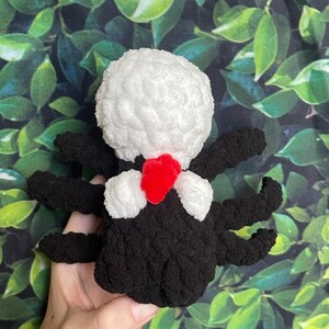 May include: A black and white crocheted spider with a red heart on its chest. The spider is sitting on a hand.