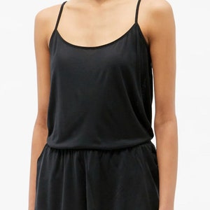 May include: A black sleeveless jumpsuit with a scoop neck and a ruffled hem. The jumpsuit is made of a soft, silky fabric.