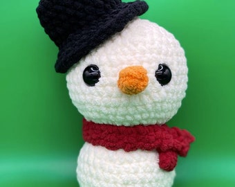 May include: A white crocheted snowman with a black top hat and a red scarf. The snowman has black eyes and an orange nose.