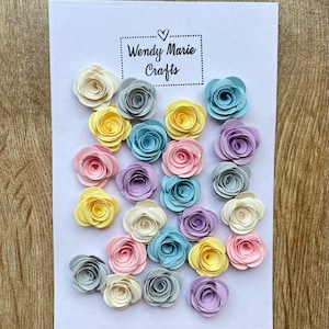 May include: A collection of 20 paper flowers in various colours, including light blue, yellow, pink, purple, and grey. The flowers are arranged in a random pattern on a white background. The text "Wendy Marie Crafts" is printed on the card.