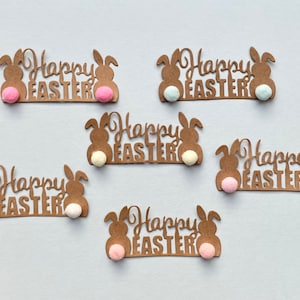 May include: Six brown paper cut-outs of bunnies with the text "Happy Easter" and pom-poms in pink, white and light blue.