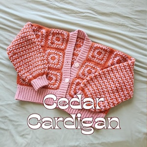 Può includere: Cardigan all'uncinetto fatto a mano nei toni dell'arancione e del rosa. Il cardigan presenta un motivo quadrato sul davanti e sulle maniche, con orlo e polsini a coste. Il testo "Cedar Cardigan" è visualizzato sul davanti.