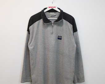 May include: A gray and black long-sleeve sweatshirt with a half-zip closure. The sweatshirt has a black collar and a black patch on the front with the letters "HS" in white.