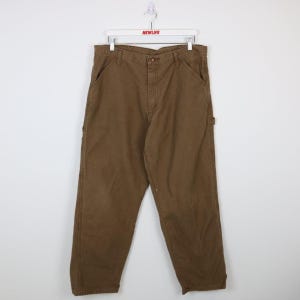 May include: Brown work trousers with multiple pockets and a button fastening. The trousers are made of a durable fabric and have a relaxed fit. The trousers are hanging on a white hanger with the word "NEWLIFE" printed on it.