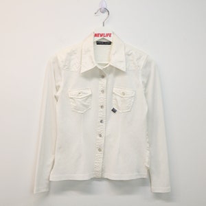 May include: An off-white long-sleeved shirt with a button-down front, two chest pockets, and a small logo. The shirt is suspended from a white hanger with the word "NEWLIFE" printed on it.