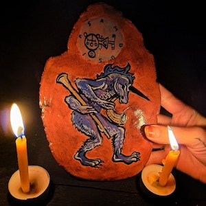 May include: A hand-painted, irregular-shaped terracotta-coloured plaque featuring a blue, furred creature with a long, pointed snout holding a staff and a horn. Above the creature is a circular emblem with the letters S, A, M, D, and T.