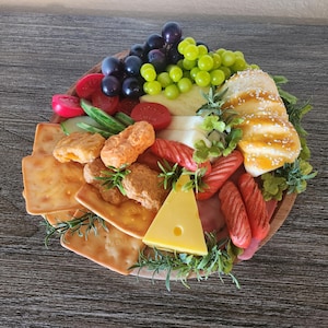 May include: A wooden charcuterie board with an assortment of food items. The board includes crackers, cheese, grapes, tomatoes, fried food, and bread. The food is arranged on a round wooden board.