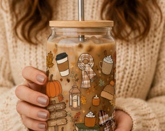 May include: A clear glass tumbler with a bamboo lid and metal straw, filled with iced coffee. The exterior features autumn-themed illustrations including pumpkins, a scarf, a lantern, a beanie, and a stack of books labeled Sweater Weather, Crisp Leaves, and Cozy Nights.
