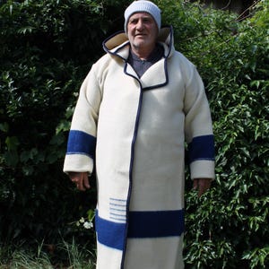 May include: A long, off-white coat with a hood and navy blue accents. The coat features a navy blue stripe around the sleeves and a similar design near the hem. The coat is made of a thick, warm material, perfect for cold weather.