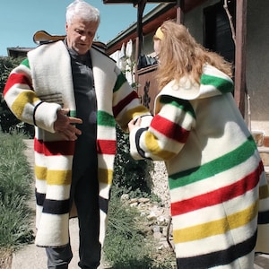 May include: Two people wearing long, white coats with colorful horizontal stripes of red, yellow, green, and black. The coats have a thick, textured appearance, and the stripes are evenly spaced. The coats appear to be made of a heavy fabric.