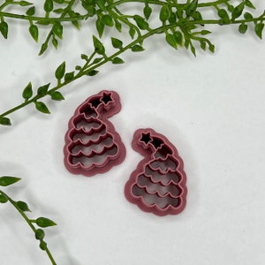 Puede incluir: Dos cortadores de galletas de plástico rosa en forma de árbol de Navidad con una estrella en la parte superior.