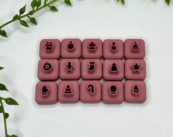 May include: A set of 16 pink plastic Christmas cookie cutters with various holiday shapes, including a Christmas tree, a star, a snowman, a stocking, a candy cane, a present, a gingerbread man, and a bell.