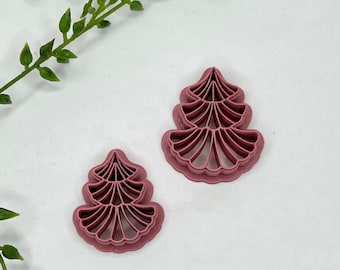 May include: Two pink plastic cookie cutters shaped like stylized trees. The cutters are detailed with multiple layers of leaves.