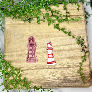 以下が含まれることがあります： ピンクと赤と白の2つの灯台の形をしたクッキーカッター。カッターは木製の表面の上に置かれています。