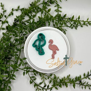 May include: Two flamingo cookie cutters, one teal and one pink, on a white background with the text "Salted Grace Co."
