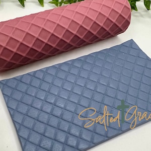 May include: A set of two silicone rolling pins with a diamond pattern. The rolling pin on the left is pink and the rolling pin on the right is blue. The blue rolling pin has the text "Salted Grace Co." printed on it.