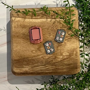 Puede incluir: Dos bandejas para hornear pequeñas con una variedad de caramelos y galletas coloridos en una tabla de cortar de madera. Las bandejas para hornear son grises con bordes rojos. La tabla de cortar es marrón con veta de madera natural.